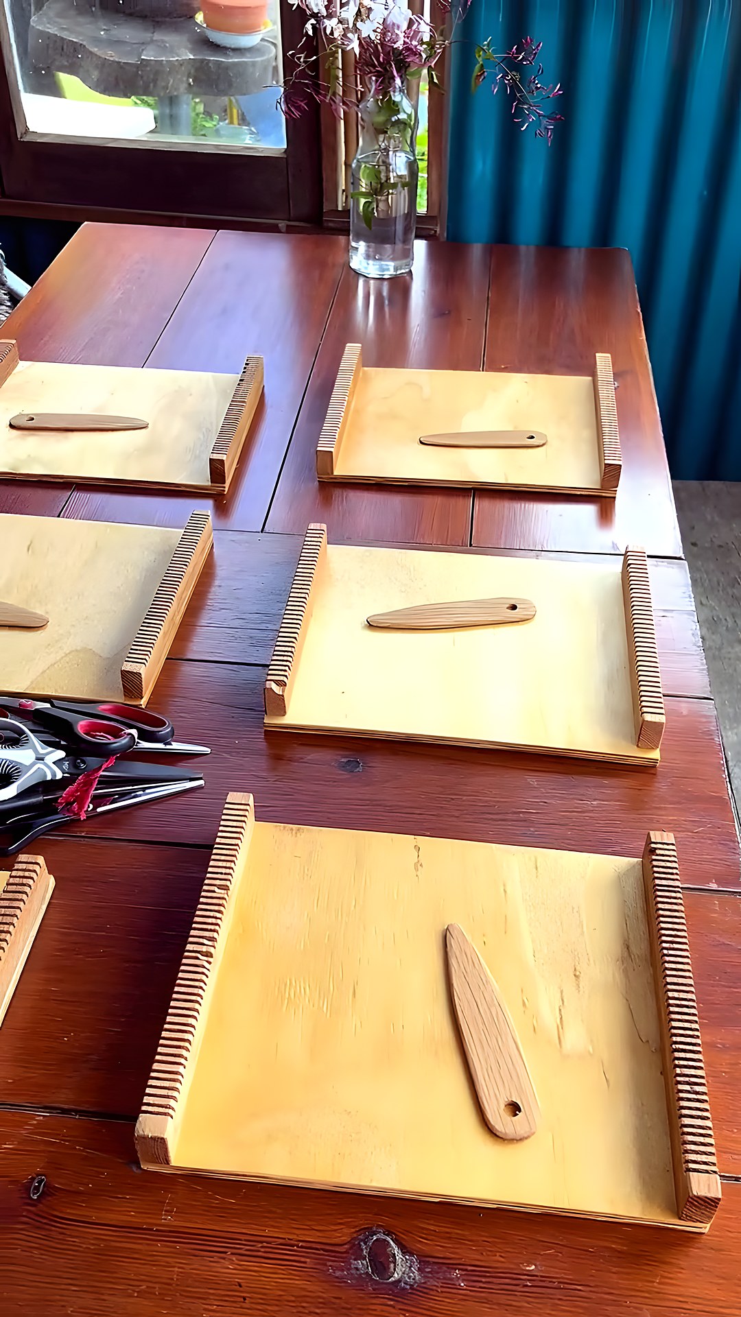 Mesa com pequenos teares de mão, preparada para um workshop